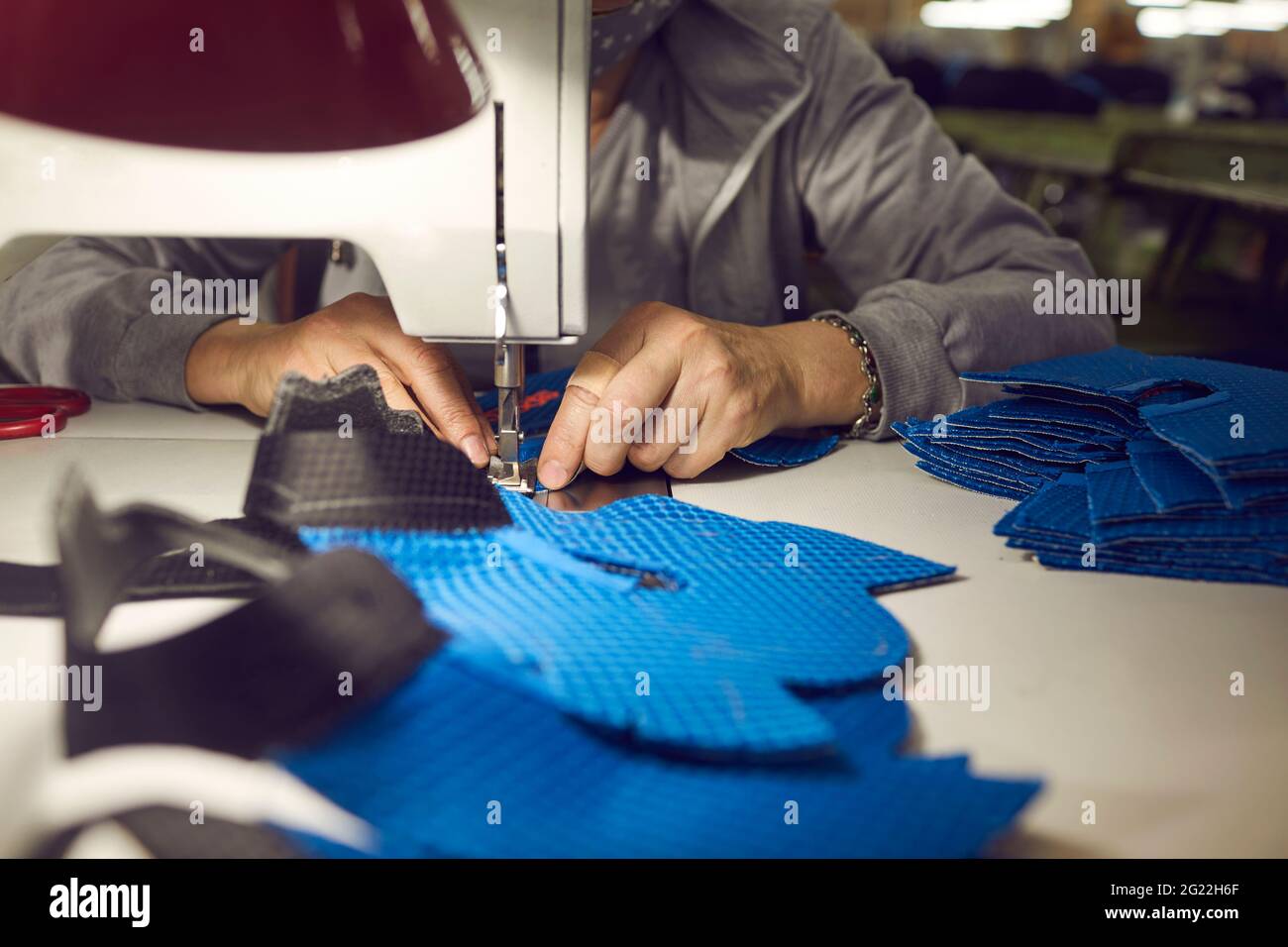 Lavoratrice femminile presso la fabbrica di scarpe che fa dettagli sneaker su macchina da cucire industriale Foto Stock