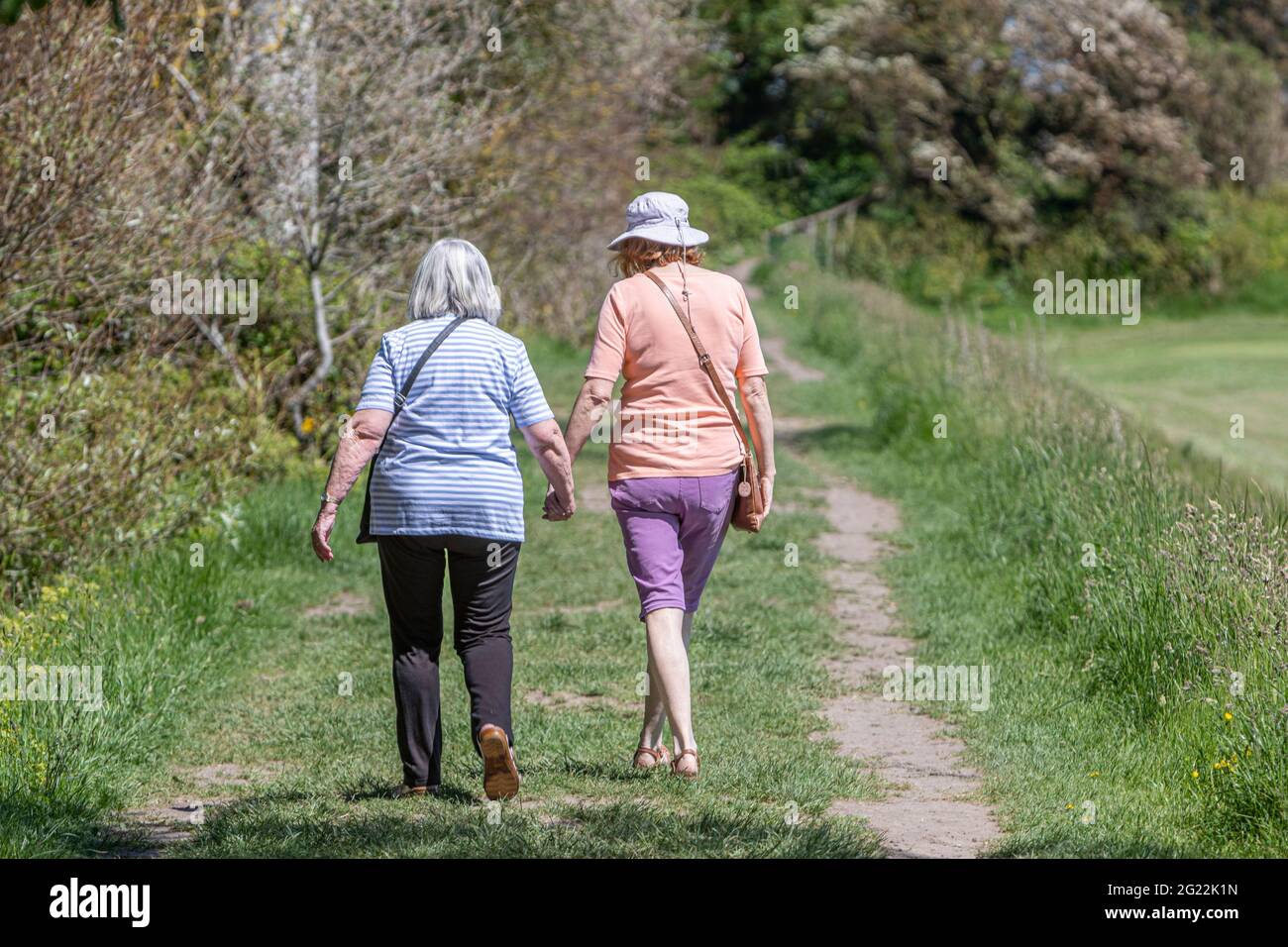 Due donne che camminano di mano in mano su un sentiero rurale Foto Stock