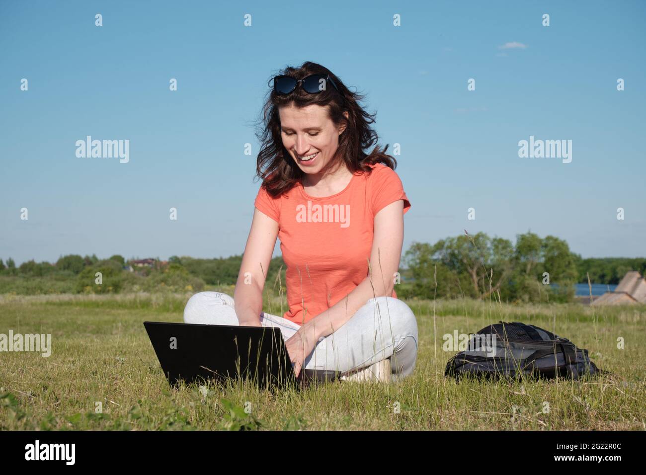 La ragazza si siede sull'erba e usa un computer portatile. Comunicazione fuori città. Circa Foto Stock