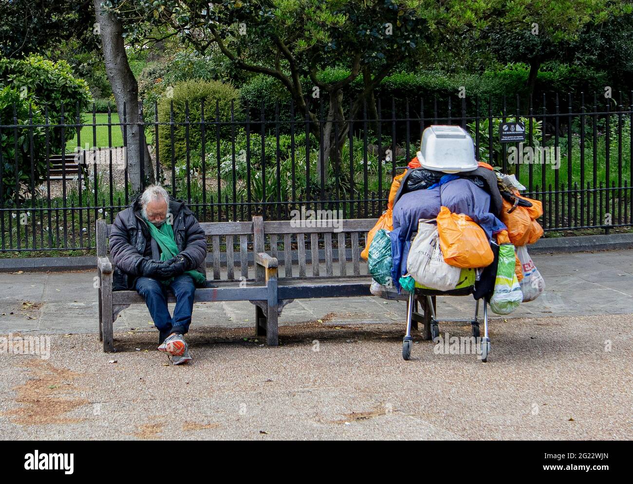 L'uomo senza dimora dormiva sulla panchina pubblica con il carrello pieno di beni a Bloomsbury Square, Holborn, Londra Foto Stock