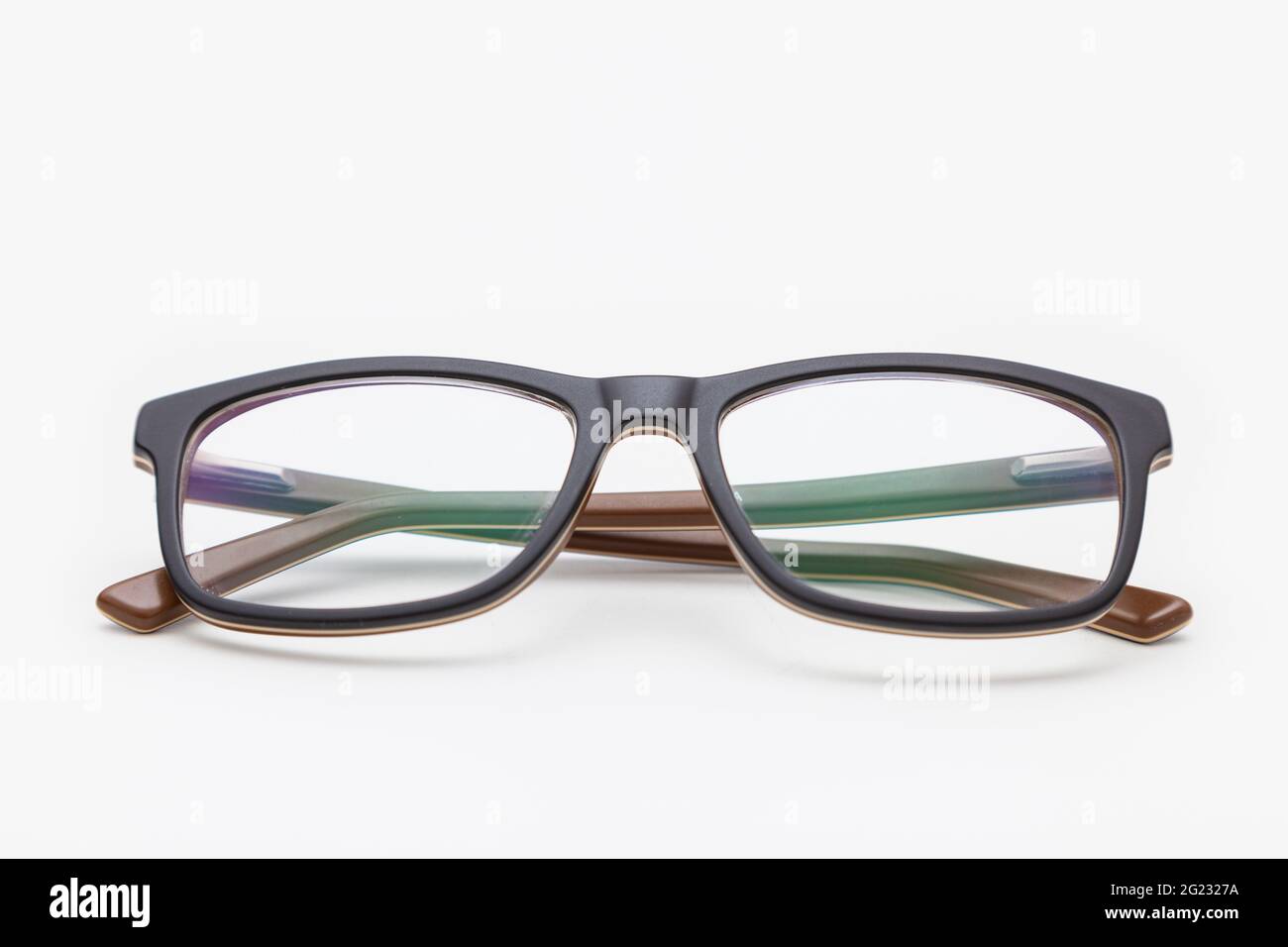 Un paio di occhiali scuri visti dalla parte anteriore, con le tempie incrociate e poste su una superficie bianca. Lo sfondo è bianco. Le basette sono se Foto Stock