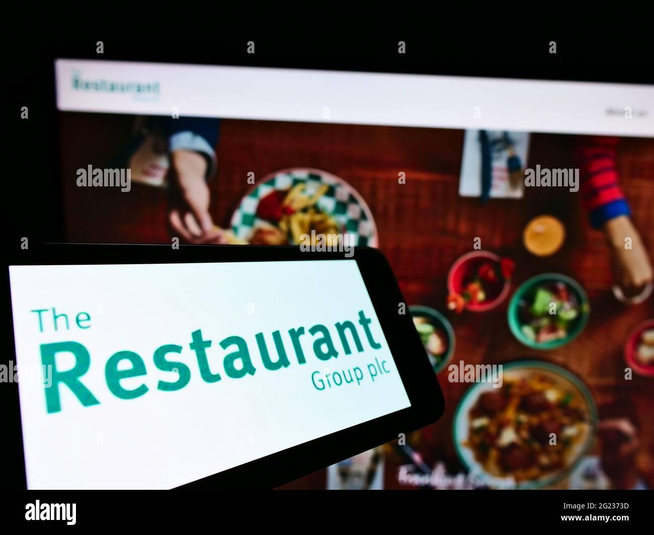 Telefono cellulare con logo della compagnia di gastronomia britannica The Restaurant Group plc sullo schermo di fronte al sito web. Mettere a fuoco il centro-destra del display del telefono. Foto Stock