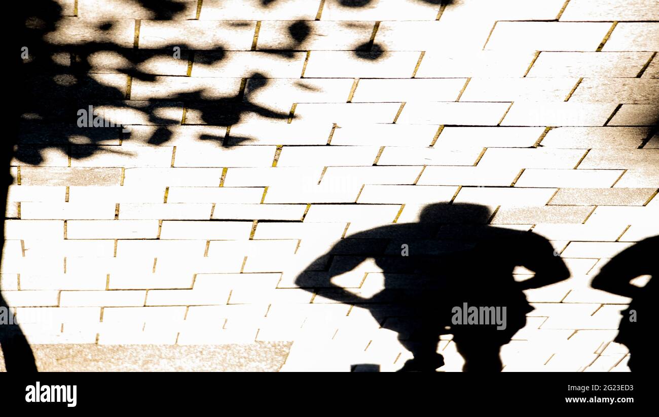 La silhouette offuscata delle ombre di una persona che cammina lungo la strada della città nella soleggiata giornata estiva, in bianco e nero Foto Stock