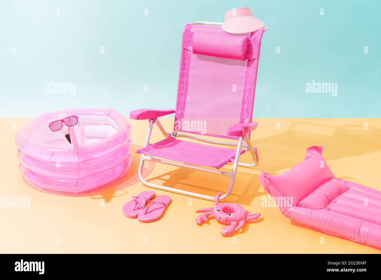 Una sedia da spiaggia rosa con infradito rosa, una visiera rosa, un tappetino gonfiabile rosa, una piscina gonfiabile rosa, un granchio gonfiabile rosa e un fla gonfiabile rosa Foto Stock