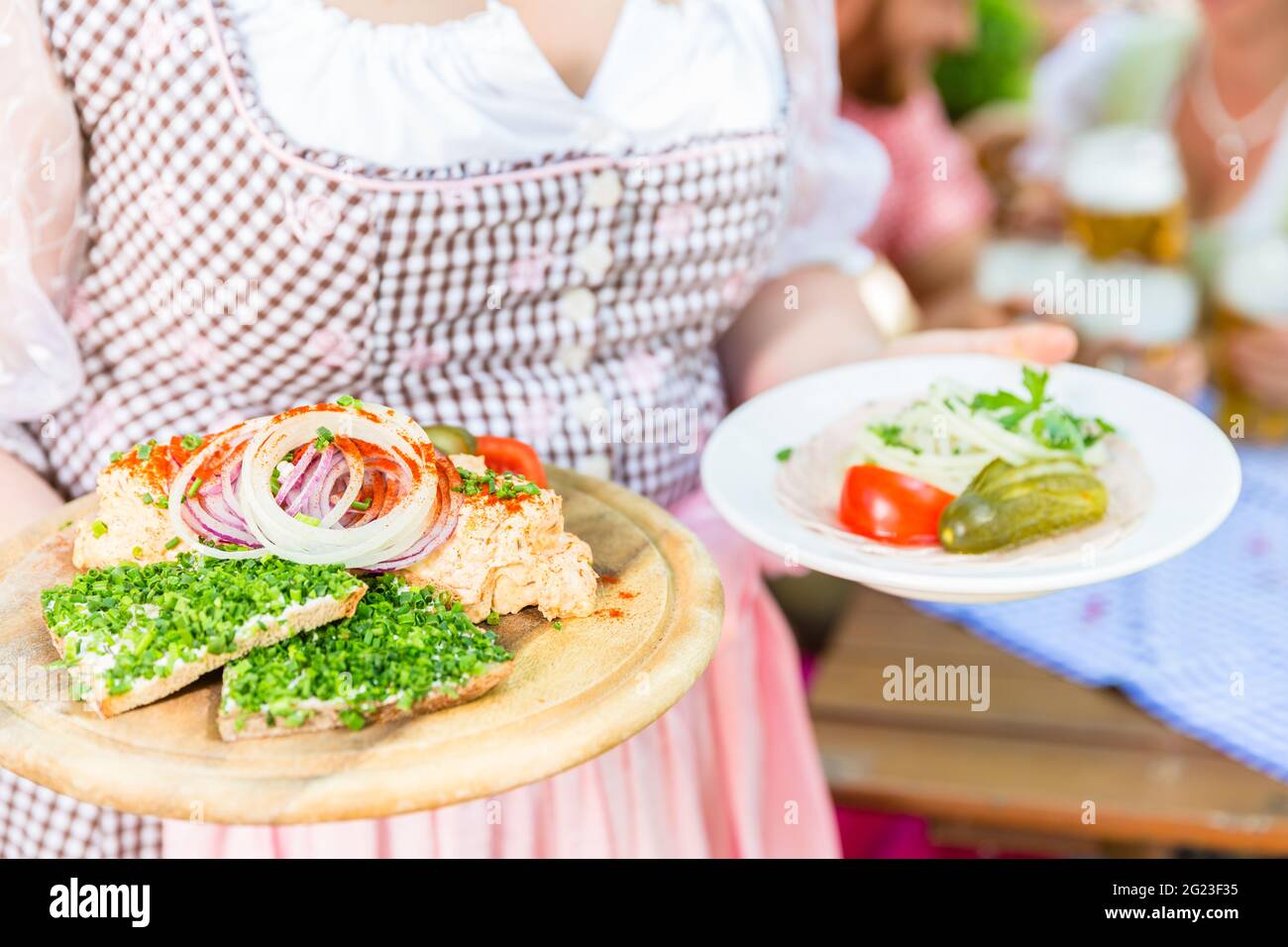 La cameriera che serve cibo bavarese nel giardino della birra, salumi, pane e obazda Foto Stock