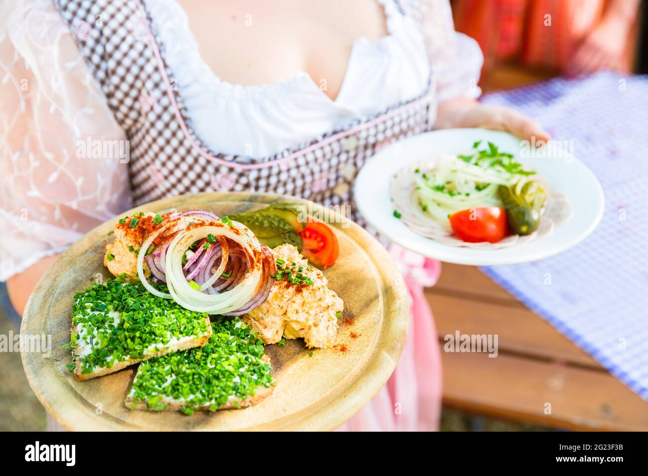 La cameriera che serve cibo bavarese nel giardino della birra, salumi, pane e obazda Foto Stock