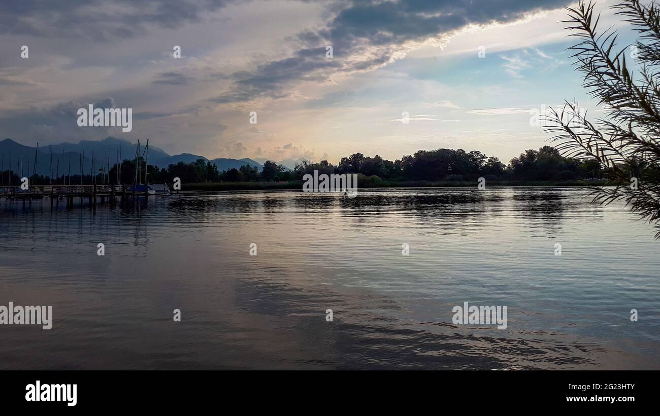 Vista panoramica del tranquillo lago Chiemsee contro il cielo serale e silhouette di alpi e alberi all'orizzonte Foto Stock