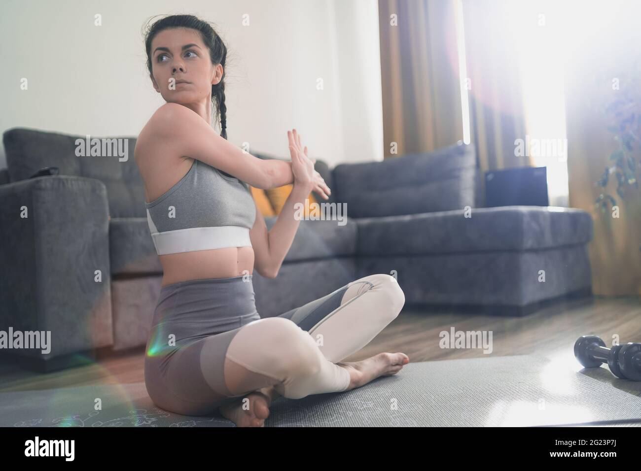 Giovane donna sportiva con reggiseno sportivo e pantaloni yoga che pratica yoga su tappetino yoga a casa Foto Stock