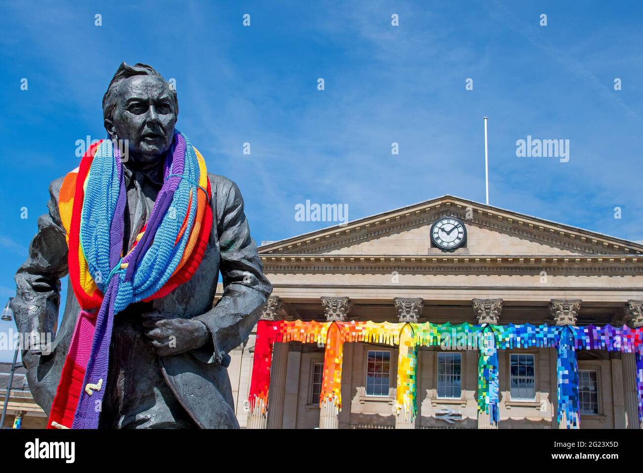 Huddersfield, Yorkshire, Regno Unito, 08 giugno 2021. La stazione ferroviaria di Huddersfield è stata bombardata dal filato. Oltre 15,000 piazze sono state lavorate da persone di tutto il mondo per coprire le sei grandi colonne sul davanti dell'edificio della stazione e persino la statua di Howard Wilson ha avuto un tocco di colore. RASQ Fotografia/Alamy. Foto Stock