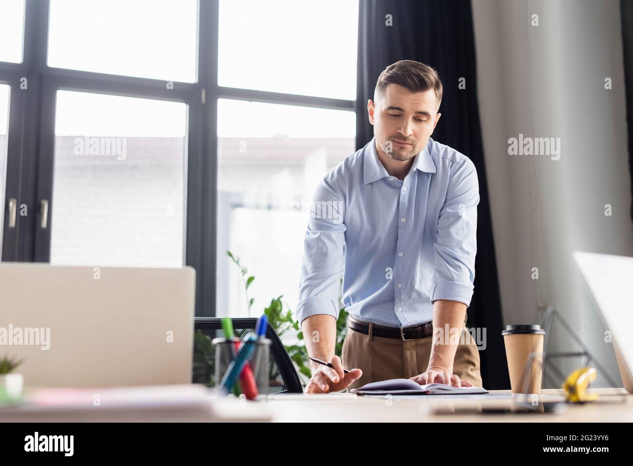 Uomo d'affari che guarda un notebook vicino a computer portatili e caffè in movimento Foto Stock