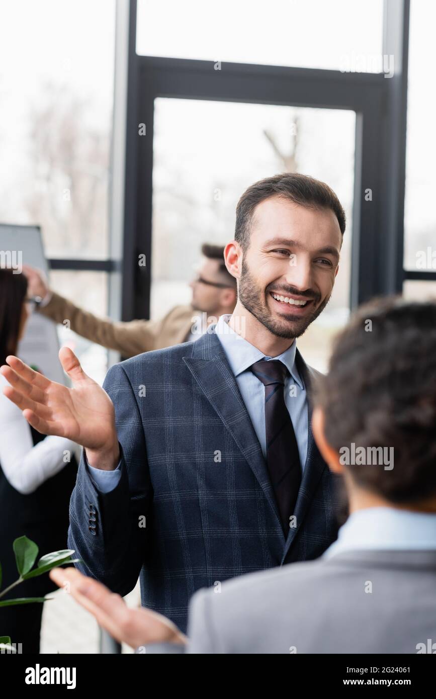 Uomo d'affari sorridente che parla con un collega offuscato in ufficio Foto Stock