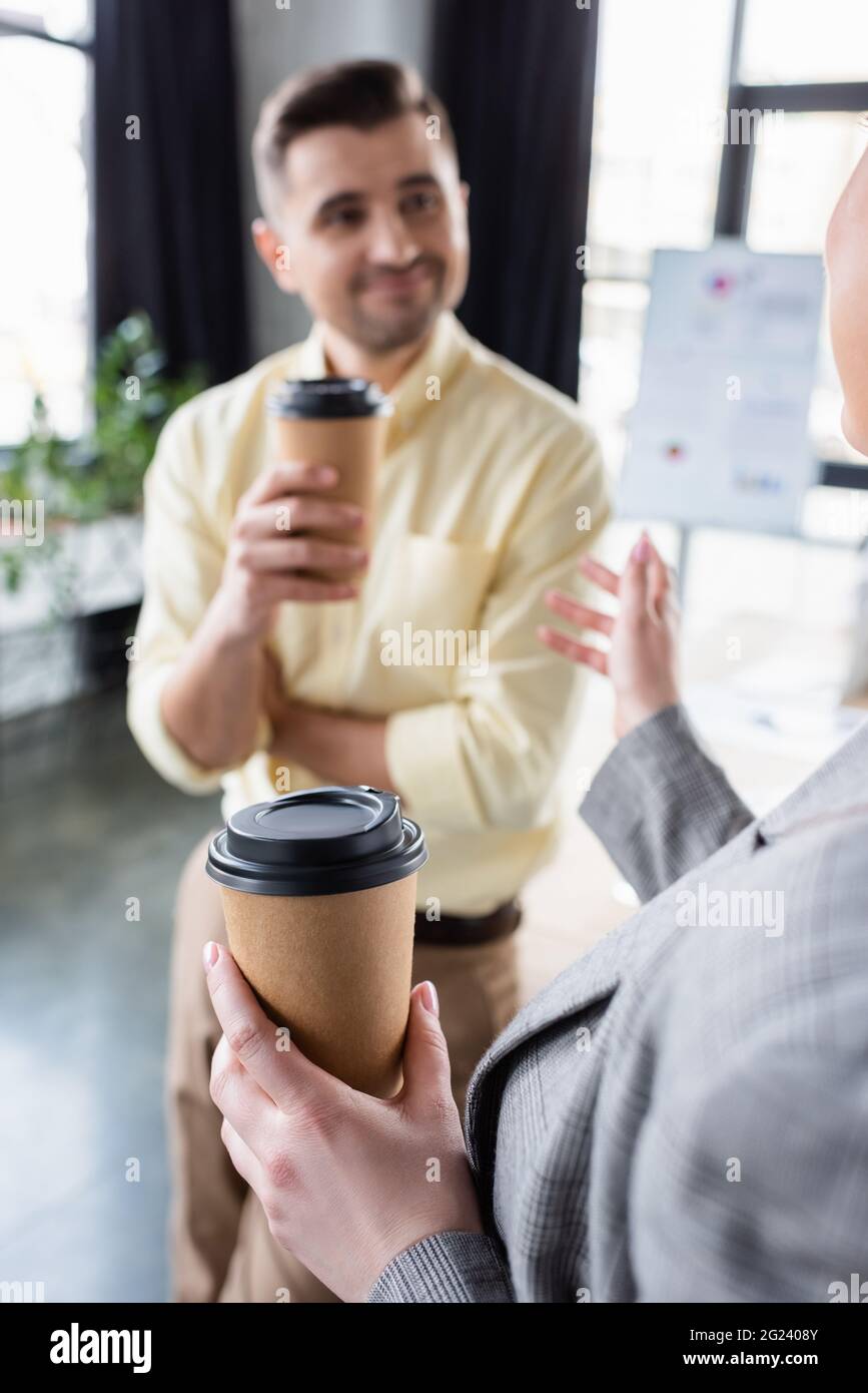 Bevanda da asporto in mano a una donna d'affari che parla con un collega offuscato in ufficio Foto Stock