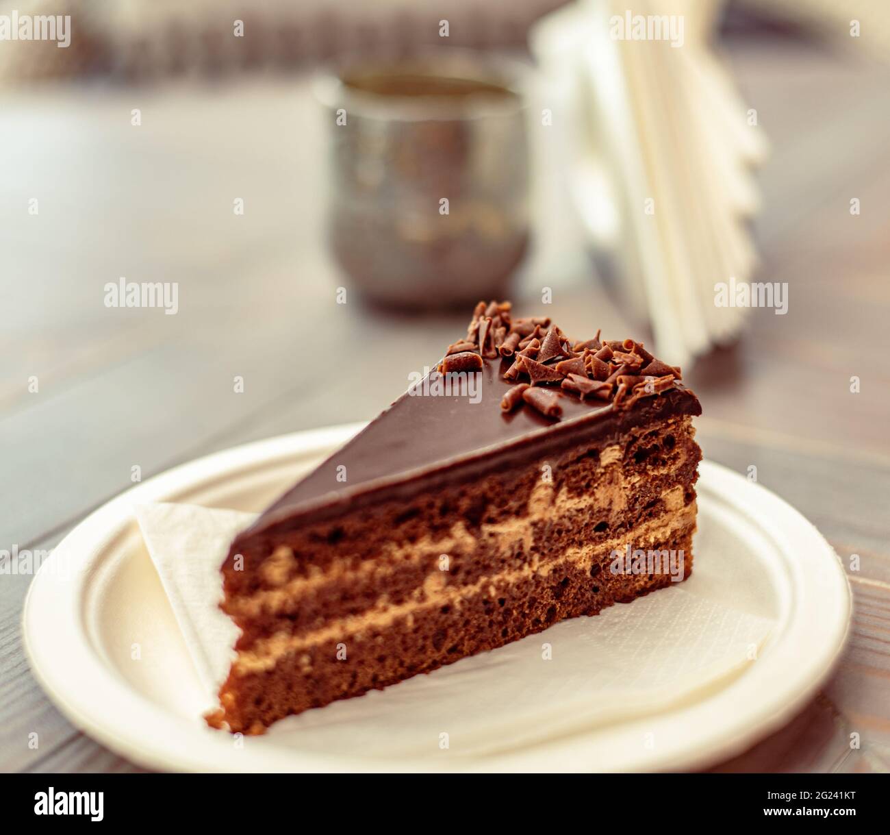 Torta multistrato al cioccolato o fetta di torta su un piatto di carta ecologico e una tazza di caffè o tè in un caffè di strada Foto Stock
