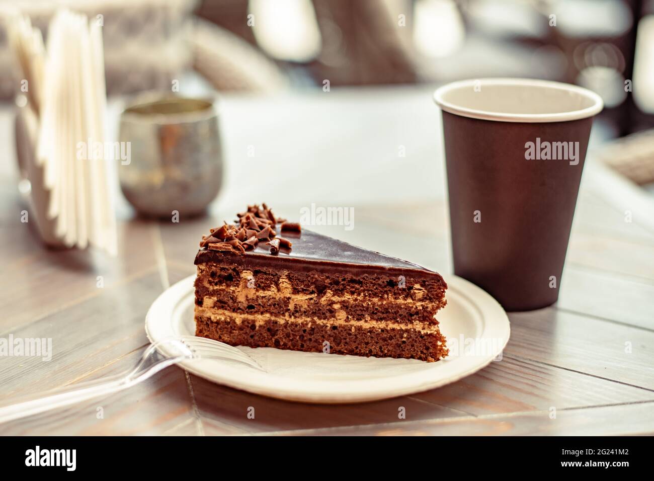 Torta multistrato al cioccolato o fetta di torta su un piatto di carta ecologico e una tazza di caffè o tè in un caffè di strada Foto Stock