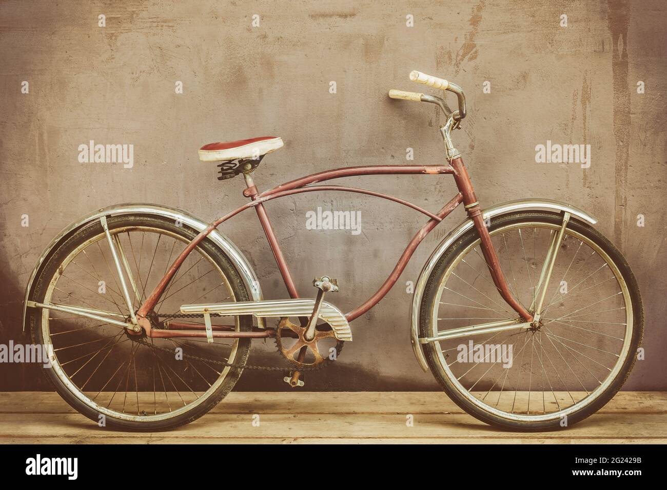 Bicicletta da crociera vintage arrugginita su un pavimento in legno con una parete di fondo intemperie Foto Stock