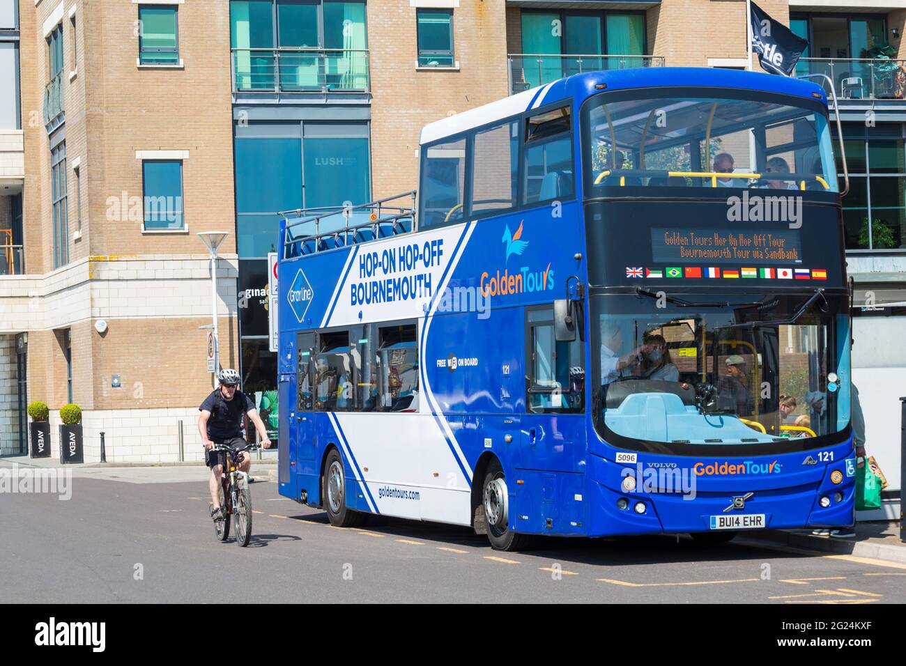 Uomo in bicicletta passando per Golden Tours Hop-on Hop-Off autobus scoperto a due piani a Poole, Dorset UK a maggio Foto Stock