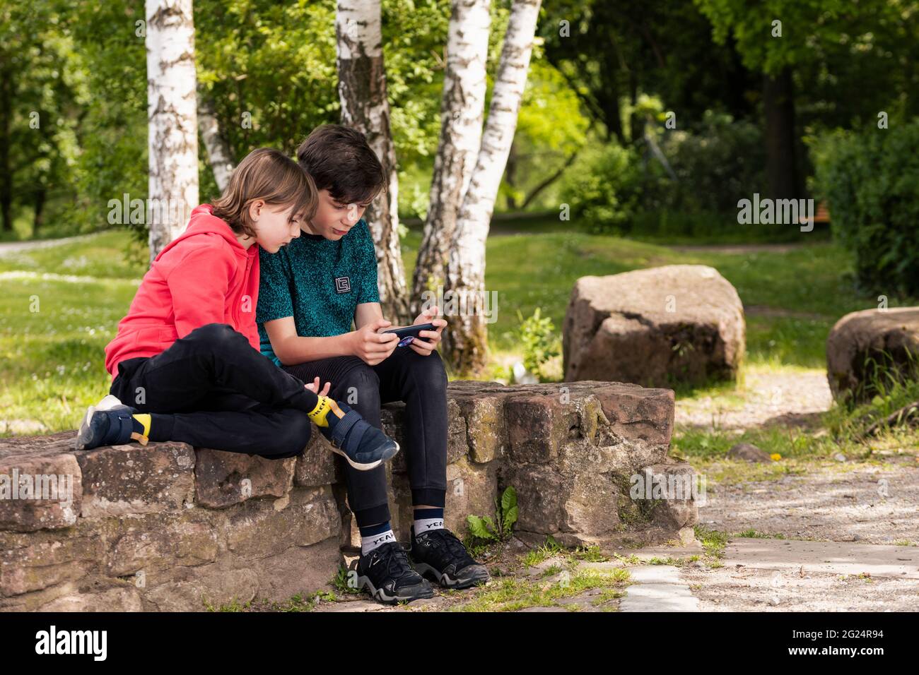 Ragazzo e ragazza seduti in un parco che guarda al telefono cellulare Foto Stock