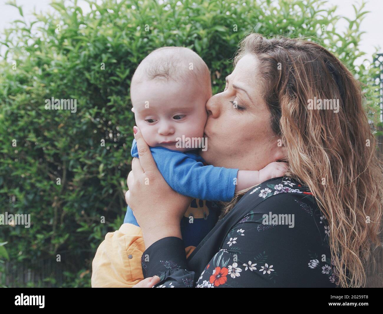 Madre in piedi nel giardino baciando il suo bambino figlio Foto Stock
