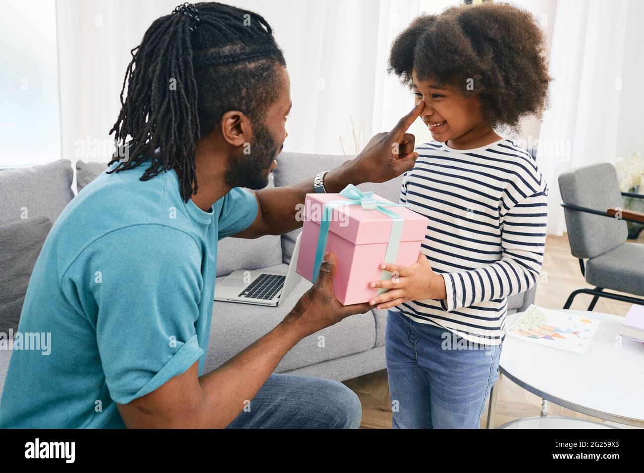 Padre dà un regalo a sua figlia per il suo compleanno. Felice African American femmina bambino con un regalo a sorpresa Foto Stock