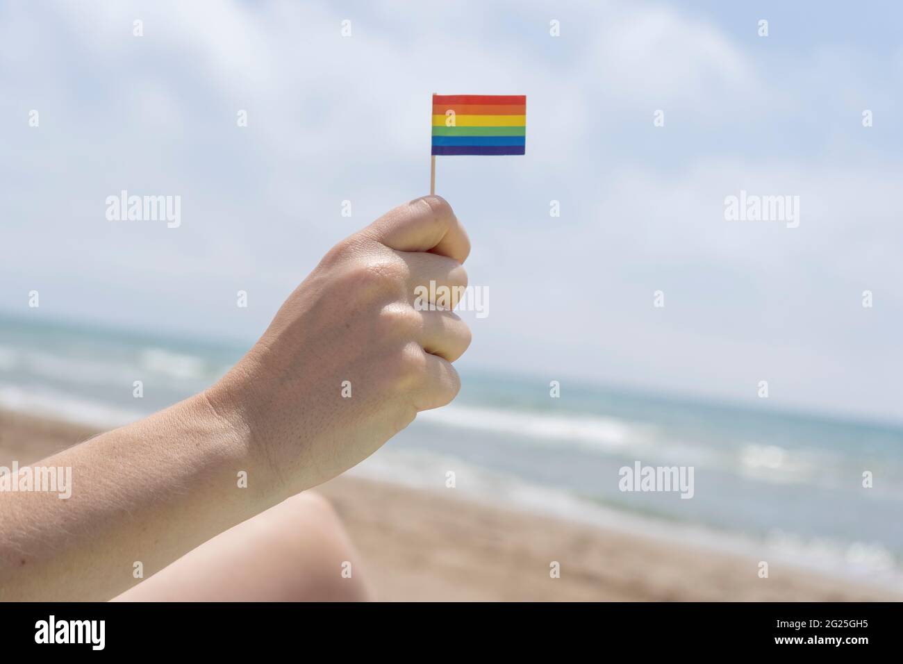 Mano che tiene una piccola bandiera arcobaleno sul concetto di orgoglio Beach.LGBTI. Foto Stock