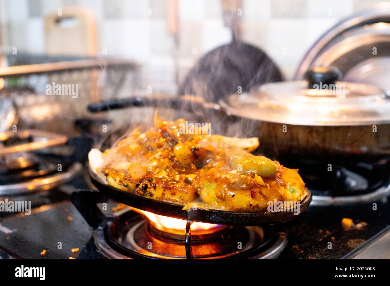 piatto vegetariano misto indiano sizzler con riso, patatine fritte, patate, cotolette di verdure e cavolo messo su piatto di ferro che viene riscaldato su una fiamma di stufa a gas Foto Stock