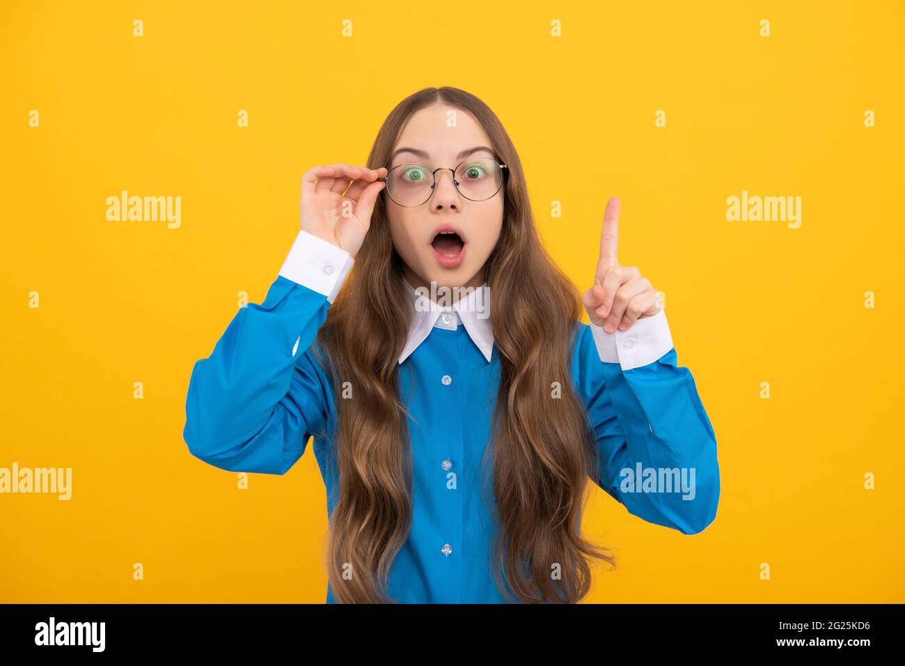 Scioccata ragazza adolescente in occhiali ha avuto genio idea mantenere sollevato dito giallo sfondo, intelligente Foto Stock