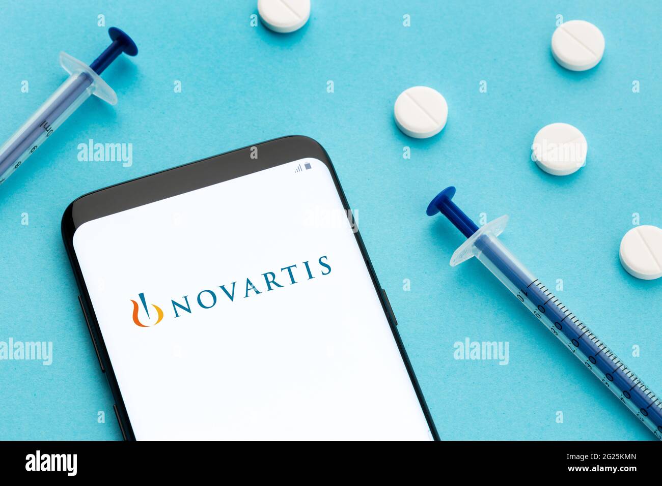 Galizia, Spagna; 8 Giugno 2020 : smartphone con logo Novartis sullo schermo e pillole e siringa su sfondo blu Foto Stock