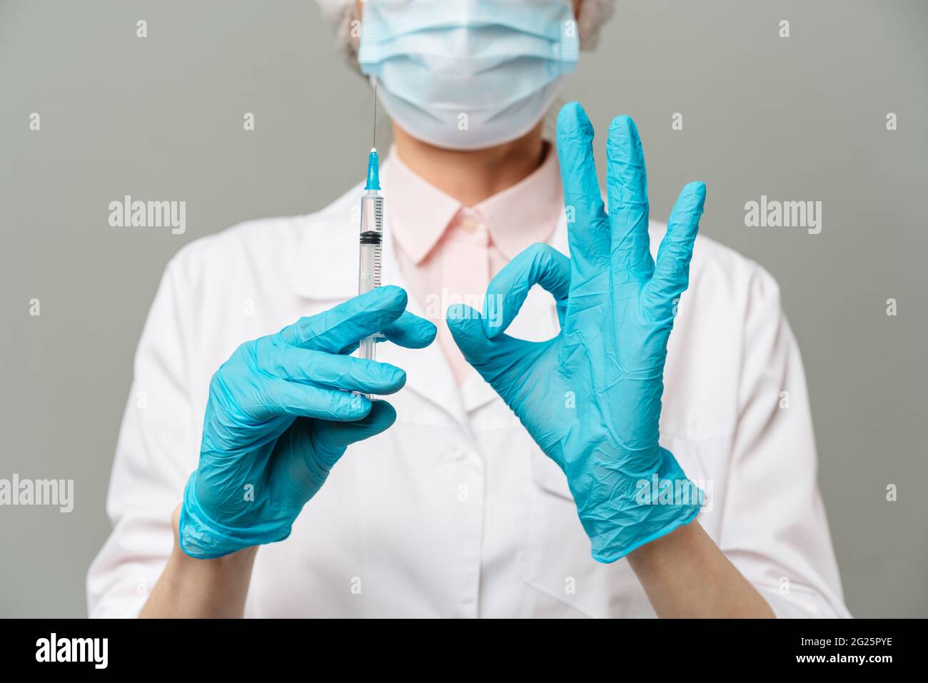Medico donna o scienziato in bianco camice blu, guanti, cappuccio verde e la maschera contiene una siringa in mani su sfondo bianco. Ella è pronta a dare Foto Stock