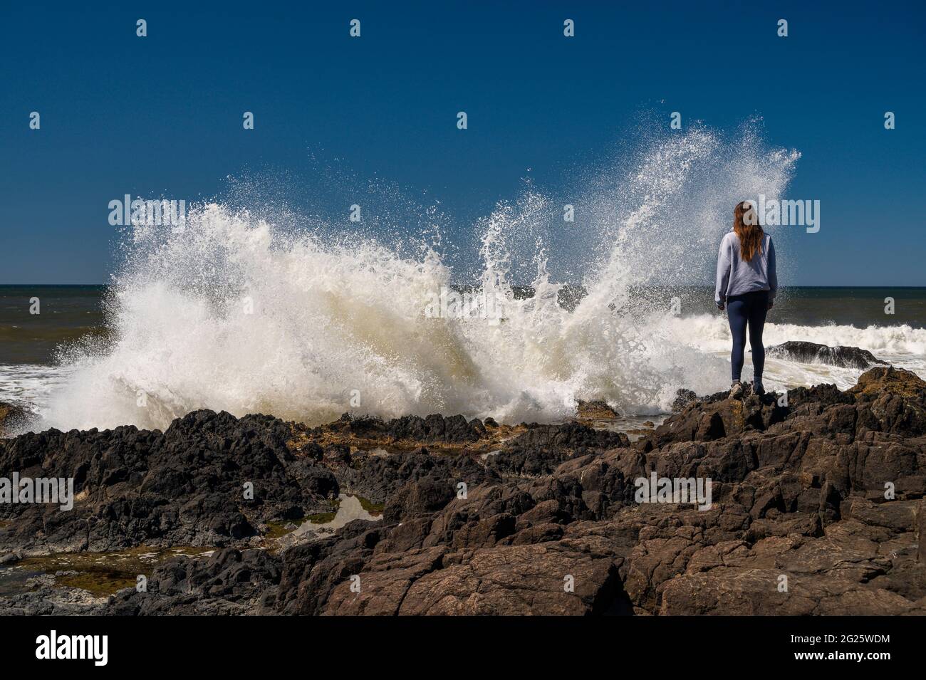 Donna in piedi sulla costa con onde che si infrangono Foto Stock
