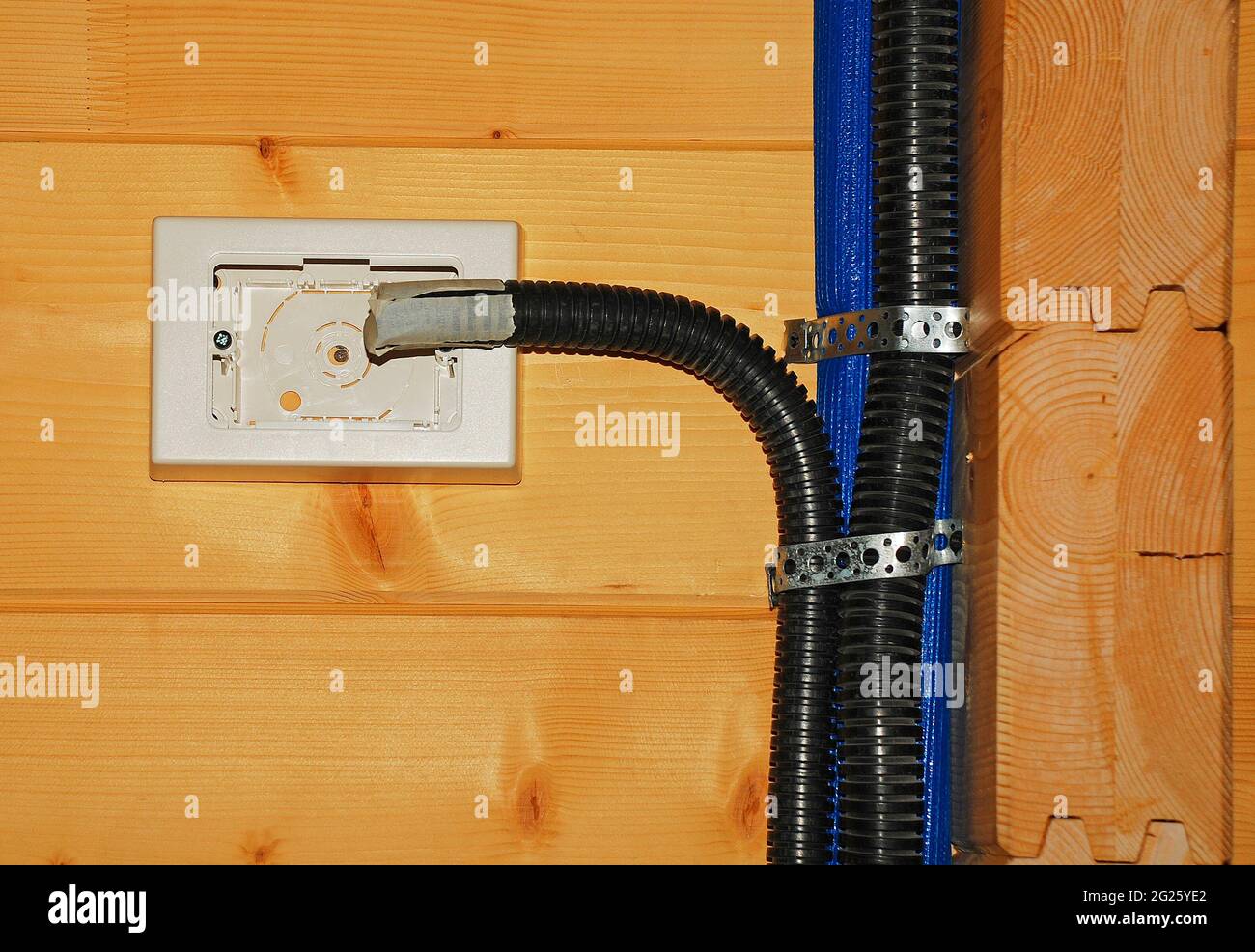 Scatola di alimentazione elettrica interna incompleta in una casa di legno per l'uso come interruttore o presa, tubo di copertura in plastica nera per la protezione del cablaggio Foto Stock