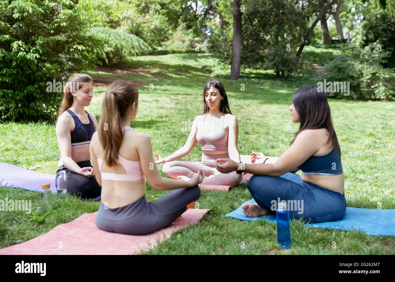 Quattro ragazze che fanno esercizi di meditazione durante la lezione di yoga all'aperto. Foto Stock