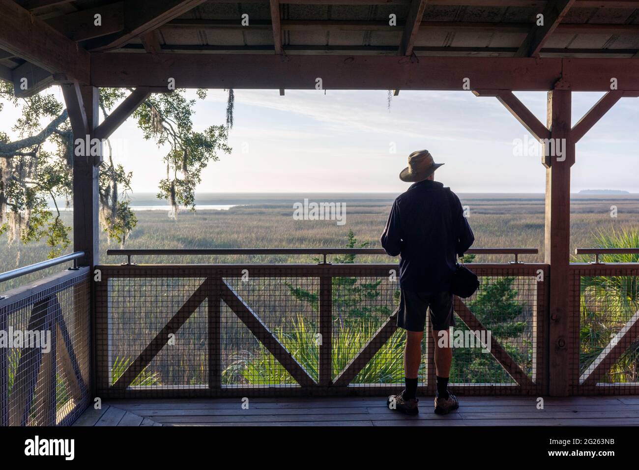 Un uomo anziano su una grande veranda si trova nello splendido sfondo paesaggistico di una palude di sale di campagna vicino all'isola di Sapelo, sulla costa della Georgia, USA. Foto Stock