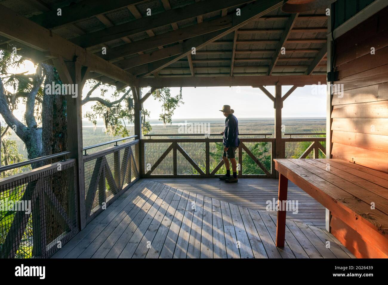 Un uomo anziano su una grande veranda si prende nel bellissimo paesaggio di una palude di sale di bassa campagna all'alba vicino all'isola di Sapelo, Georgia costiera, Stati Uniti. Foto Stock