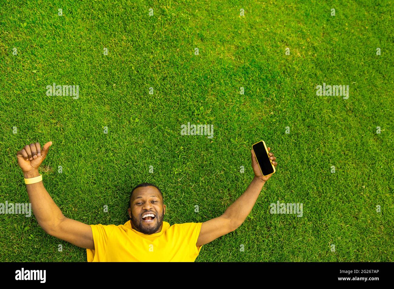 Vista dall'alto di un allegro maschio afroamericano che festeggia la vittoria, la corsa di successo, la partita o la partita di calcio. Giovane afro adagiato sull'erba Foto Stock