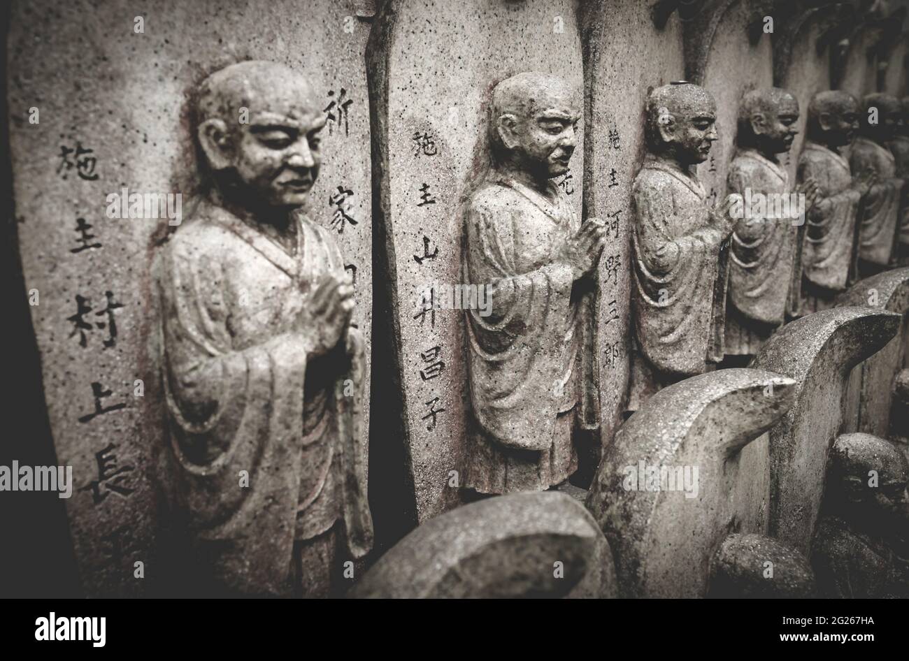 Fuoco selettivo sulle statue buddiste di pietra con testo giapponese in una linea al tempio di Daisho-in a Miyajima, Hiroshima, Giappone Foto Stock