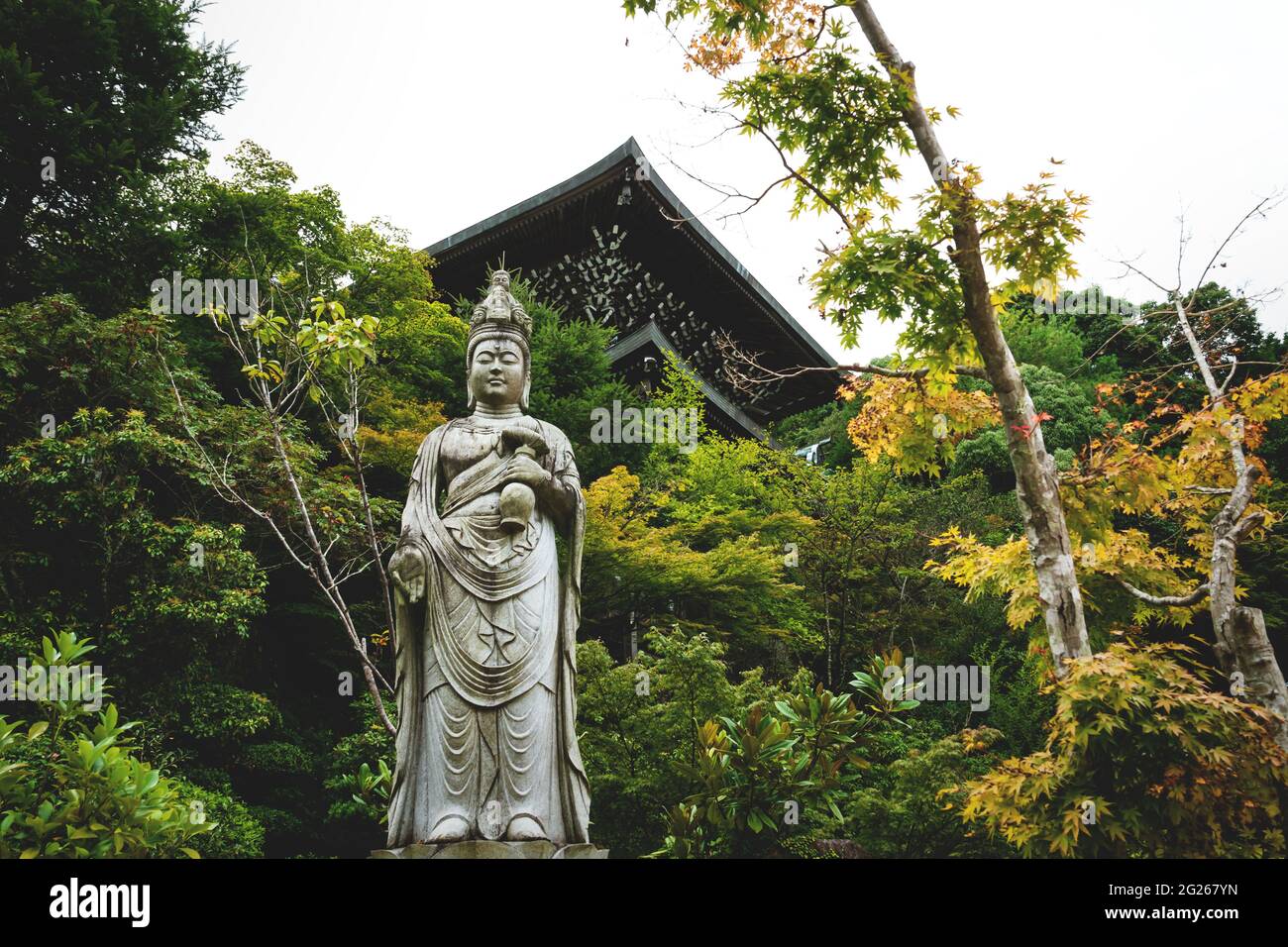 Statua buddista tra santuari e alberi autunnali colorati al tempio di Daisho-in a Miyajima, Hiroshima, Giappone Foto Stock