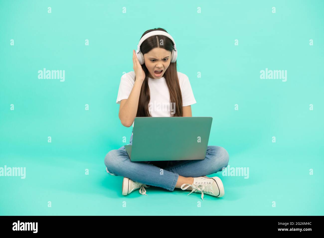 scioccato bambino ragazza influencer utilizzare il computer per videochiamata o ascoltare webinar in cuffia, blogging. Foto Stock