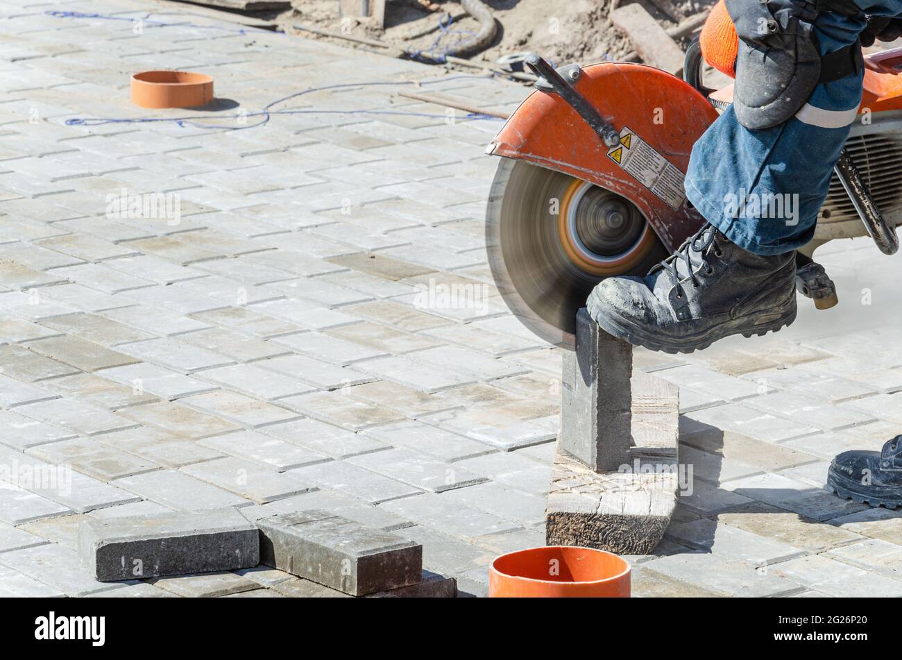 Un lavoratore taglia lastre di pavimentazione con una taglierina a gas e. una sega a mano Foto Stock