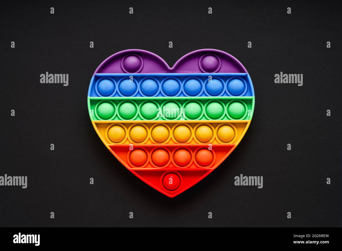 Colorato trendy Pop IT cuore forma fidgets giocattolo per bambini su uno sfondo nero. Giocattolo antistress, sviluppo delle capacità motorie di mani e dita, Foto Stock