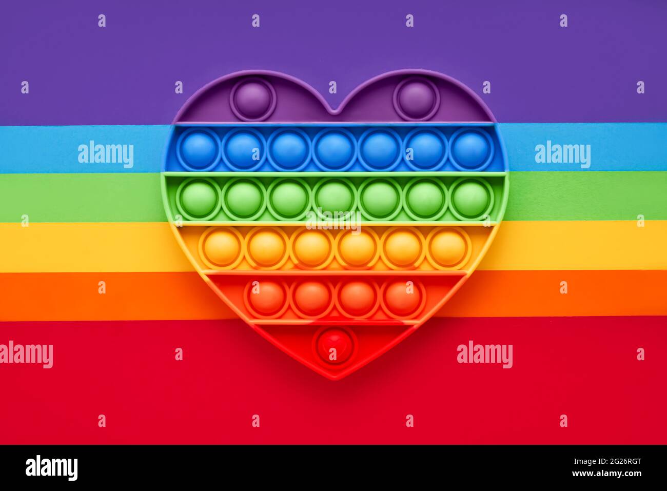 Colorato trendy Pop IT cuore forma fidgets giocattolo per bambini su uno sfondo arcobaleno. Giocattolo anti-stress, sviluppo delle capacità motorie di mani e dita Foto Stock