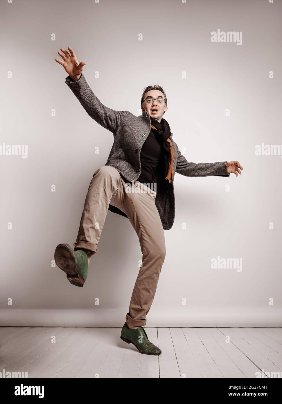 L'uomo adulto in pantaloni e giacca di plaid sta tenendo il piede in su, facendo il passo gigante, cadendo giù le mani che ondolano Foto Stock