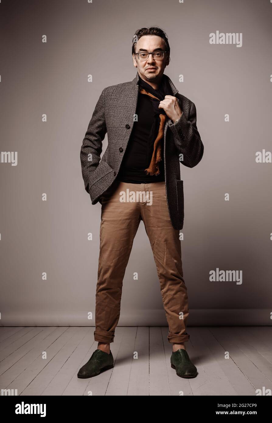 Hipster uomo adulto di stile ottimista in pantaloni e giacche di plaid tiene la mano in tasca e togli la sciarpa Foto Stock