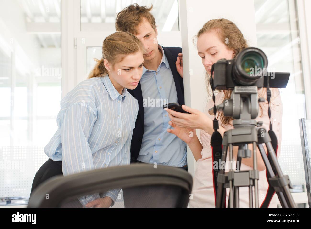 Gruppo di giovani colleghi creativi in piedi vicino al treppiede con fotocamera professionale e discutere le foto sul telefono cellulare mentre lavorano insieme in moderno Foto Stock