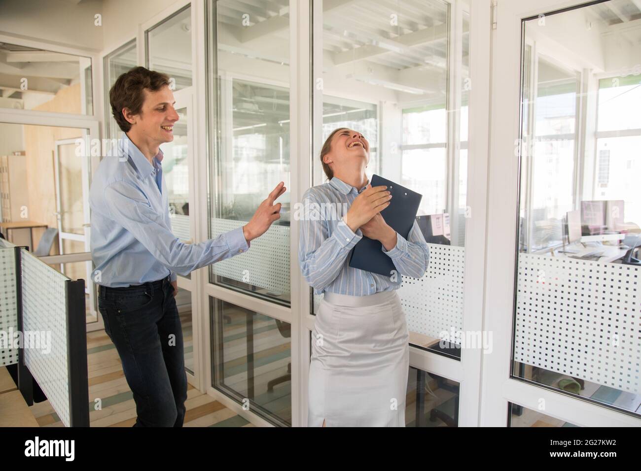 Sorridente lavoratore maschio mostrando le dita incrociate a una collega femminile con appunti ridendo gioiosamente in ufficio Foto Stock