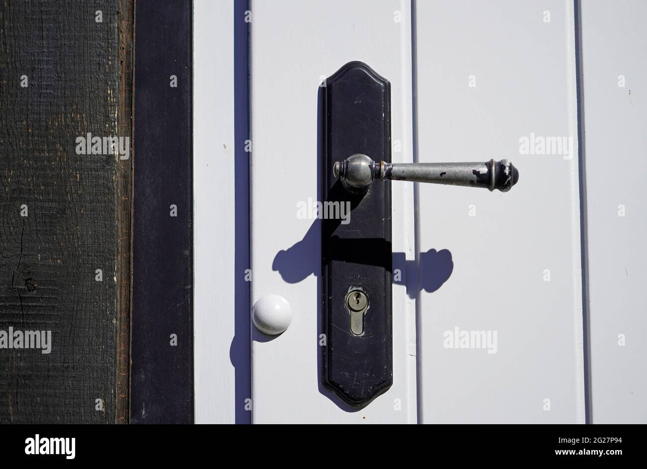 Vecchia maniglia in metallo nero su una porta di legno bianco. Primo piano dello sportello bloccato con foro per chiave. Foto Stock