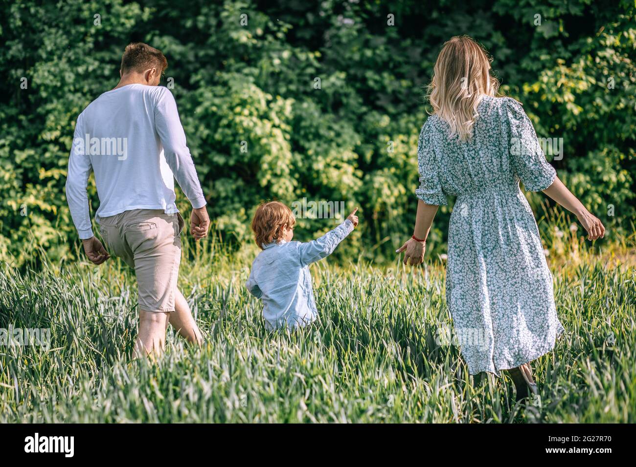 Famiglia che tiene le mani con il bambino, vista posteriore, Madre, Padre che cammina all'aperto, due genitori sono in campo agricolo, foto Foto Stock