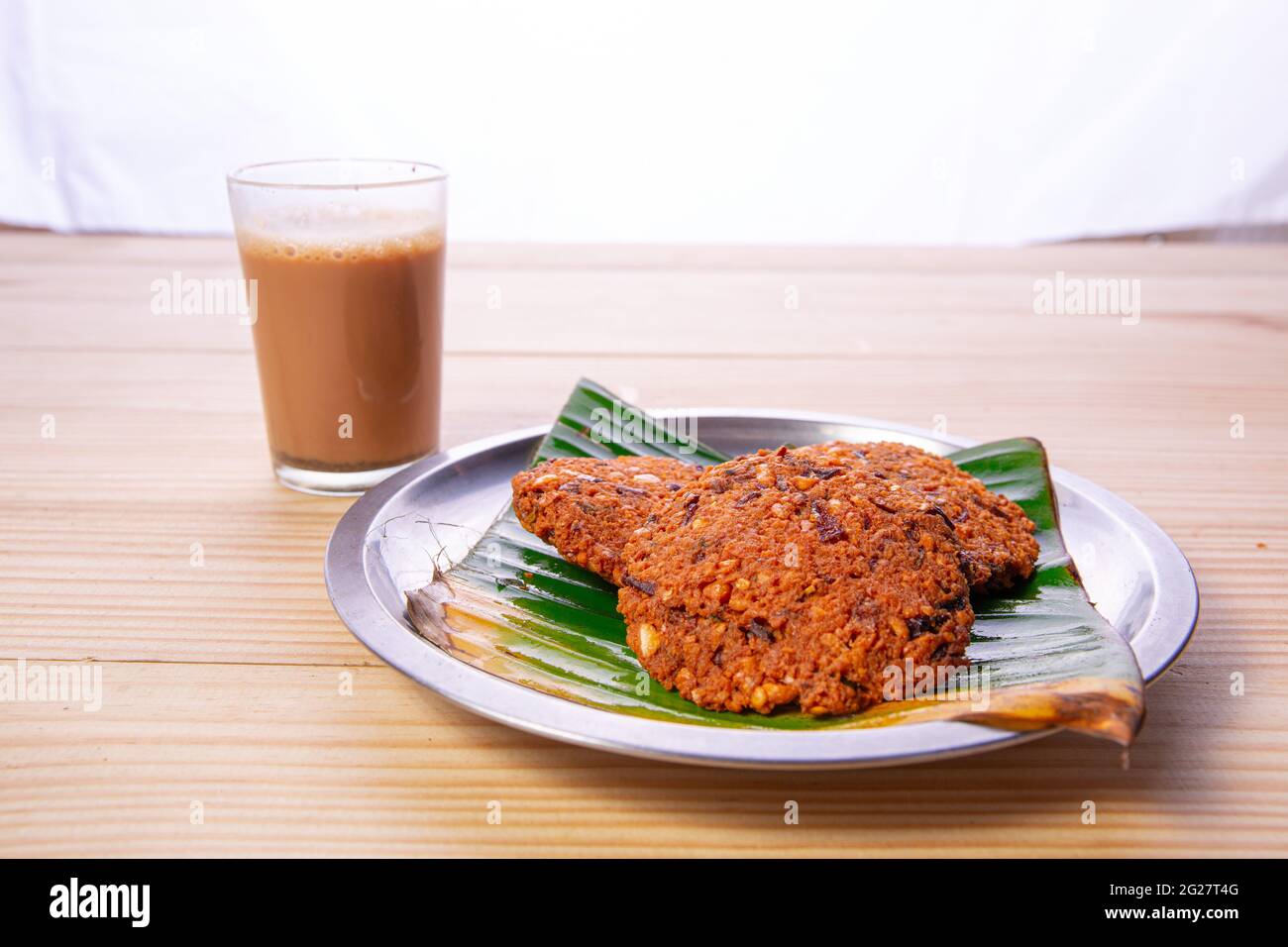 Parippu vada o Lentil Fritters, disposti tradizionalmente in una piastra di acciaio rivestita con foglia di banana e un bicchiere di tè accanto ad esso con legno testurizzato bac Foto Stock