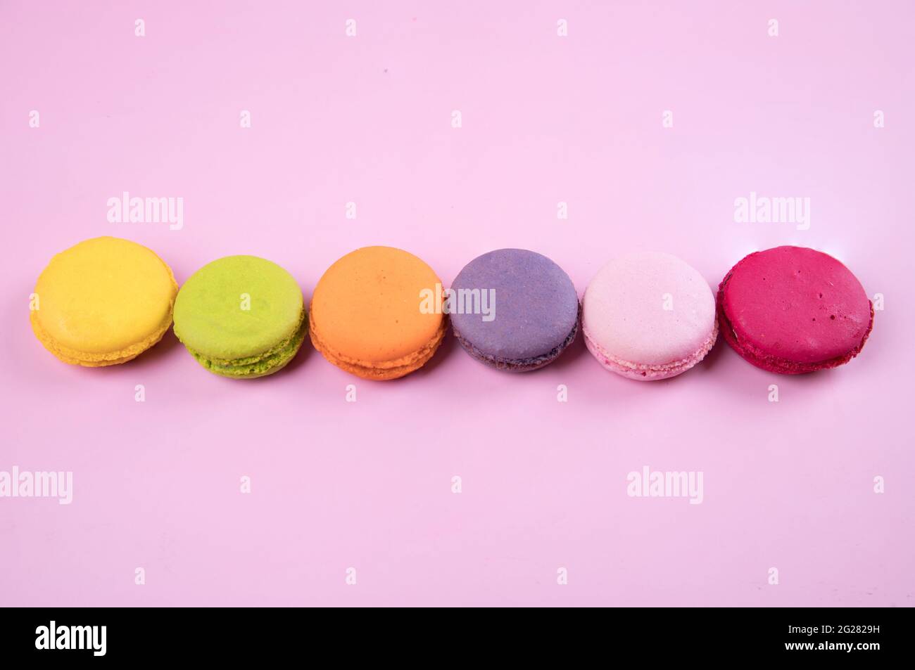 Allineati in una fila di biscotti color pastello macaroon su uno sfondo di carta rosa. Foto Stock
