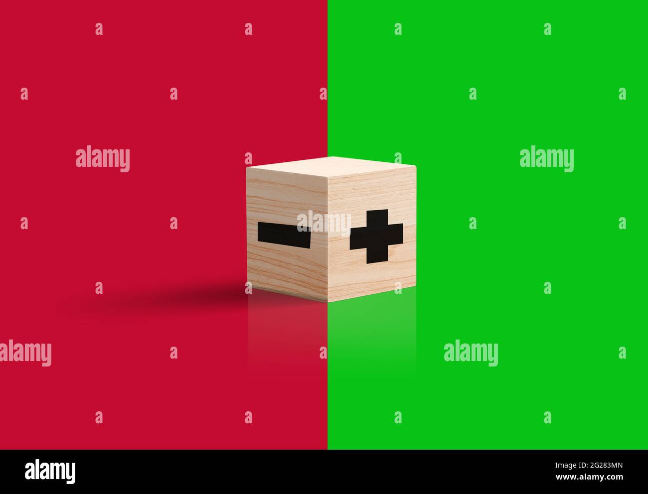 Segno più e meno su cubo di legno. Concetto di opzione negativo o positivo. Sfondo verde e rosso. Foto Stock