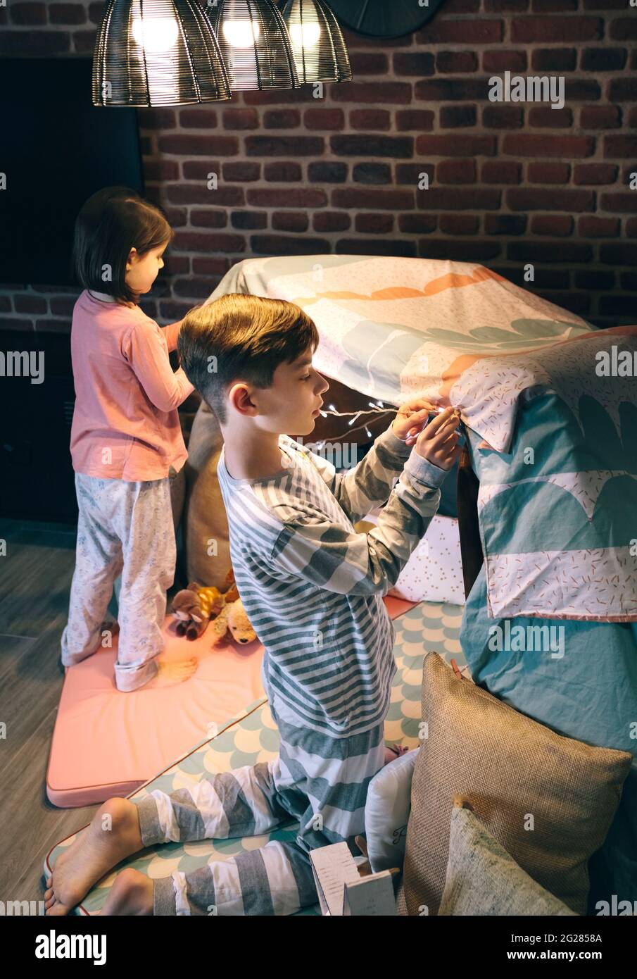 Ragazzo che aiuta la sorellina che mette un ghirlanda di luci in una tenda per una festa di sonno Foto Stock